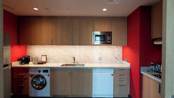 A compact kitchen with wooden cabinets, a built-in microwave, a washing machine, and a dishwasher.