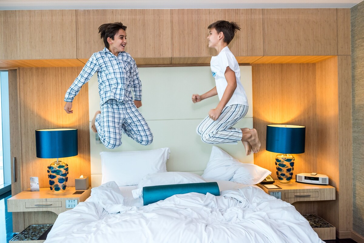 A hotel room with a bed, two bedside tables with lamps, a nightstand, and a window.