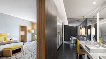 A modern hotel bathroom with a large mirror, dual sinks, a bathtub, and a yellow chair.