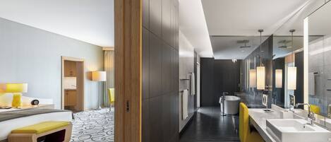 A modern hotel bathroom with a large mirror, dual sinks, a bathtub, and a yellow chair.