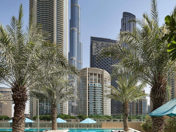 A pool area with palm trees and modern high-rise buildings in the background.