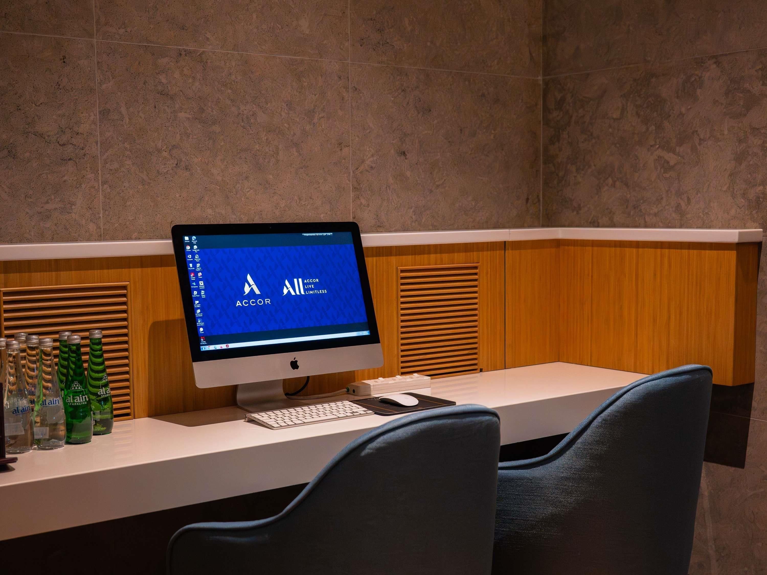 Un escritorio con un monitor de computadora que muestra el logotipo de ACCOR, un teclado, un ratón y una botella de agua con gas Alain.
