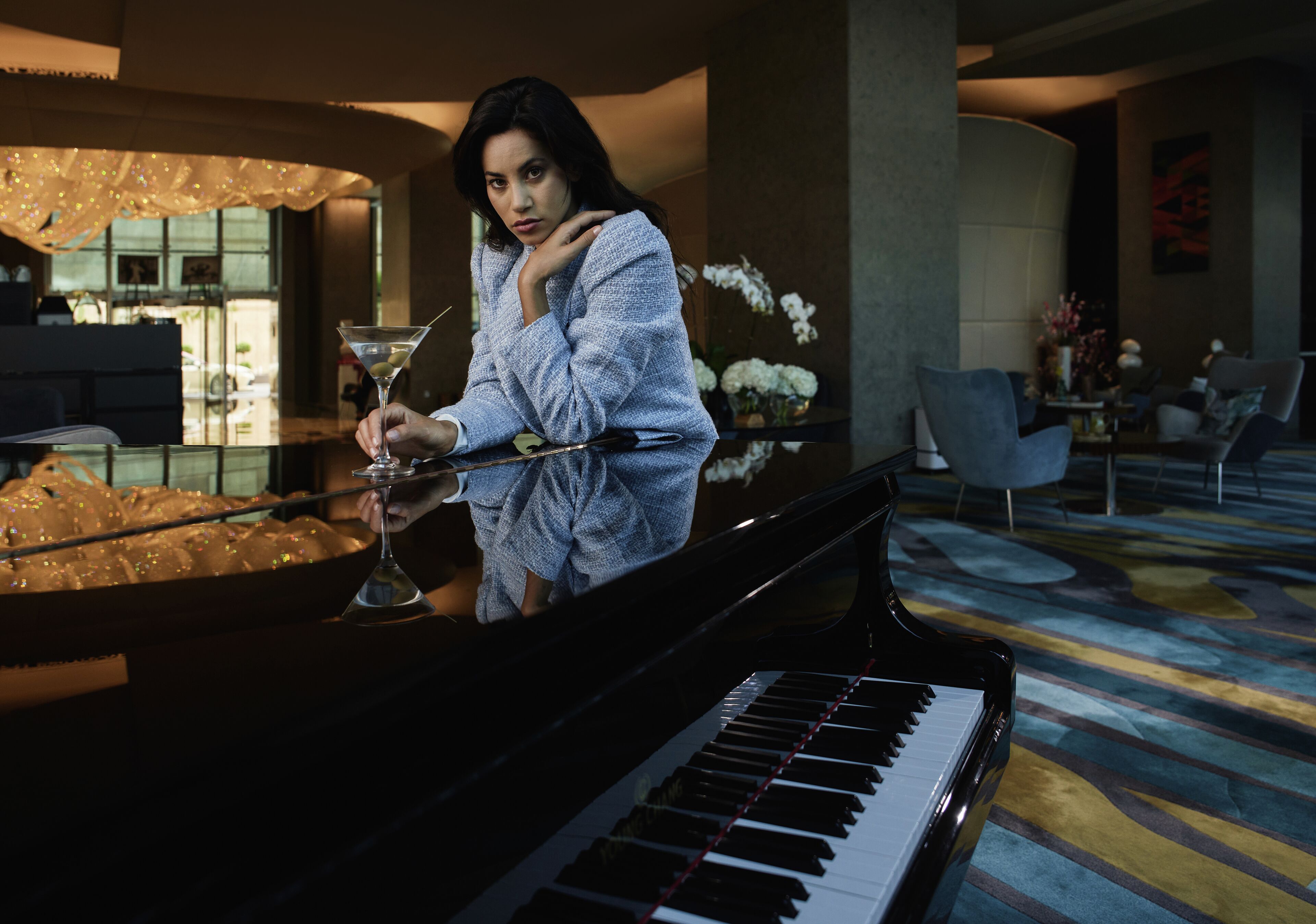 Une femme joue d’un piano à queue dans une pièce bien éclairée, dont le décor intérieur est moderne, avec un sol recouvert de moquette et des meubles contemporains.