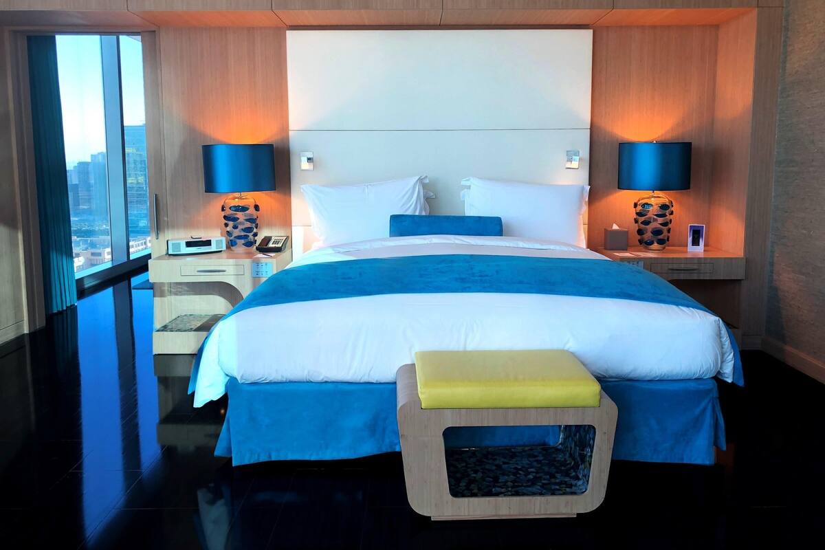 A hotel room with a large bed, bedside lamps, a nightstand, and a view of the city.