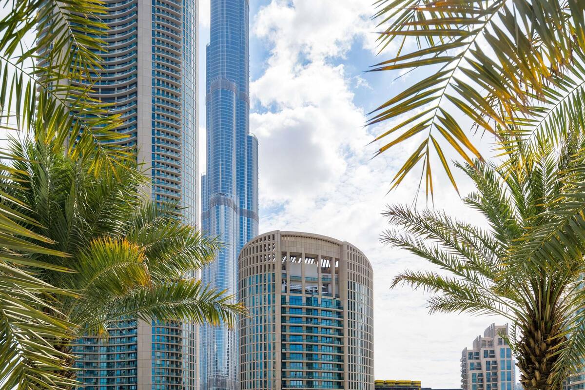 A tall skyscraper with a curved facade, surrounded by palm trees and other modern buildings.