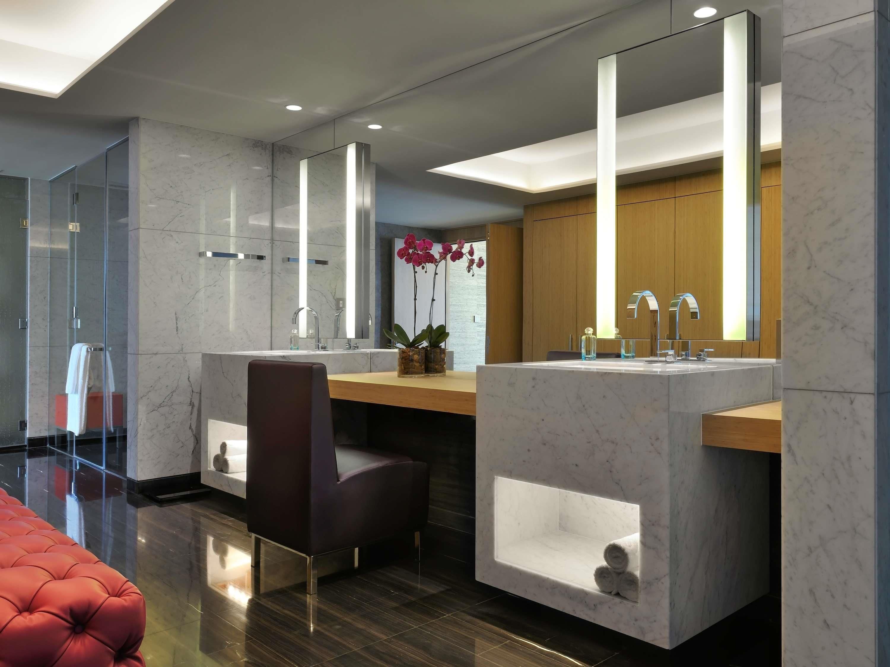 Une salle de bain moderne avec un meuble-lavabo en marbre, une cabine de douche en verre et un fauteuil rouge recouvert de tissu.