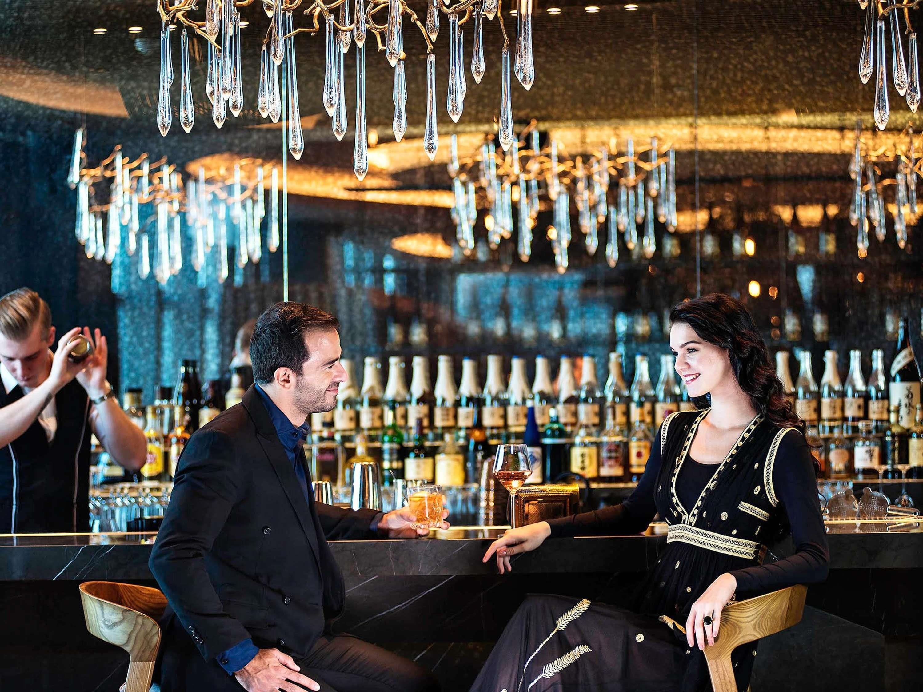 A bar setting with a bartender, a seated man, and a woman.