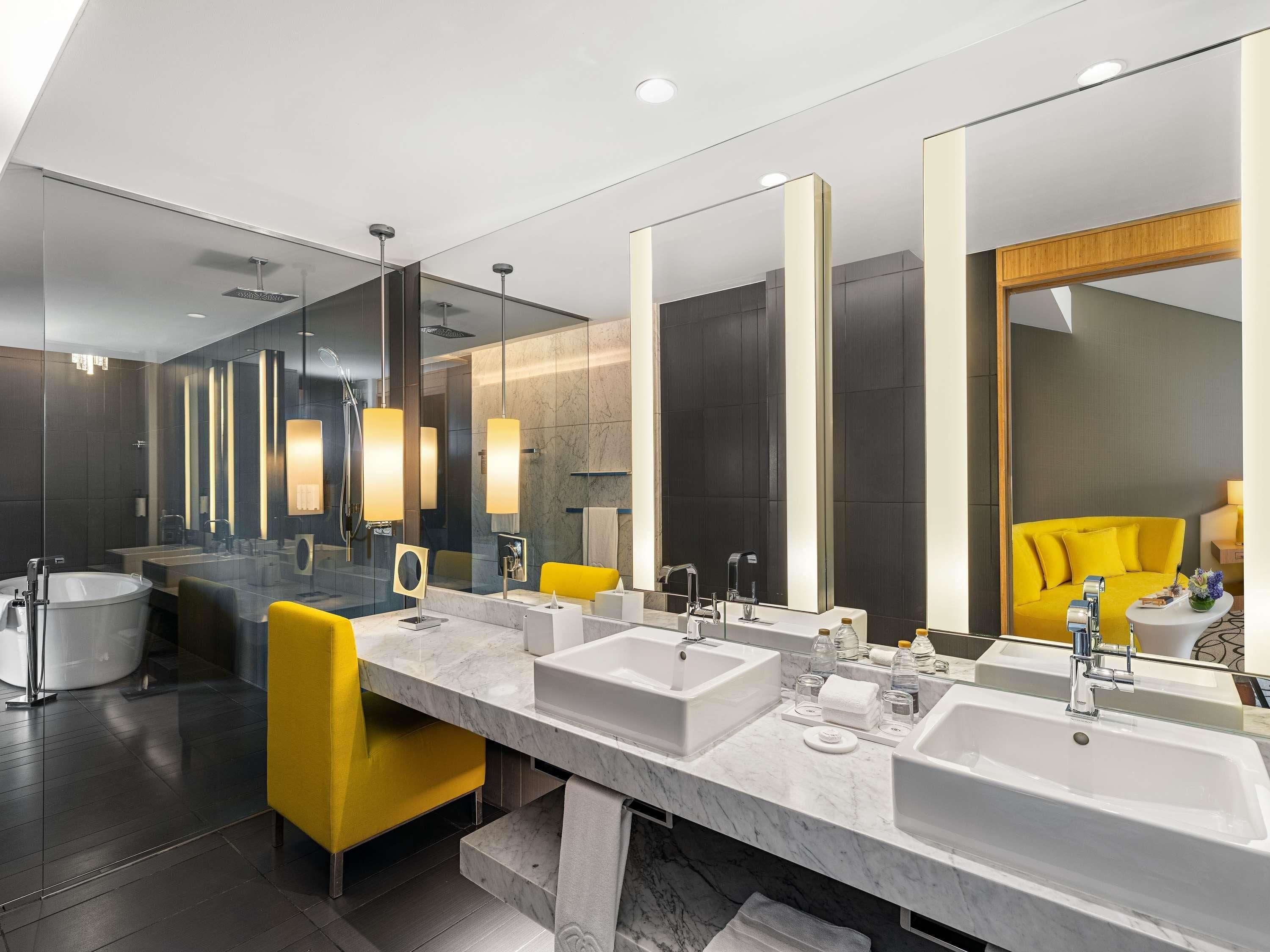 Une salle de bain moderne avec un grand miroir, deux lavabos, une baignoire et une chaise jaune.