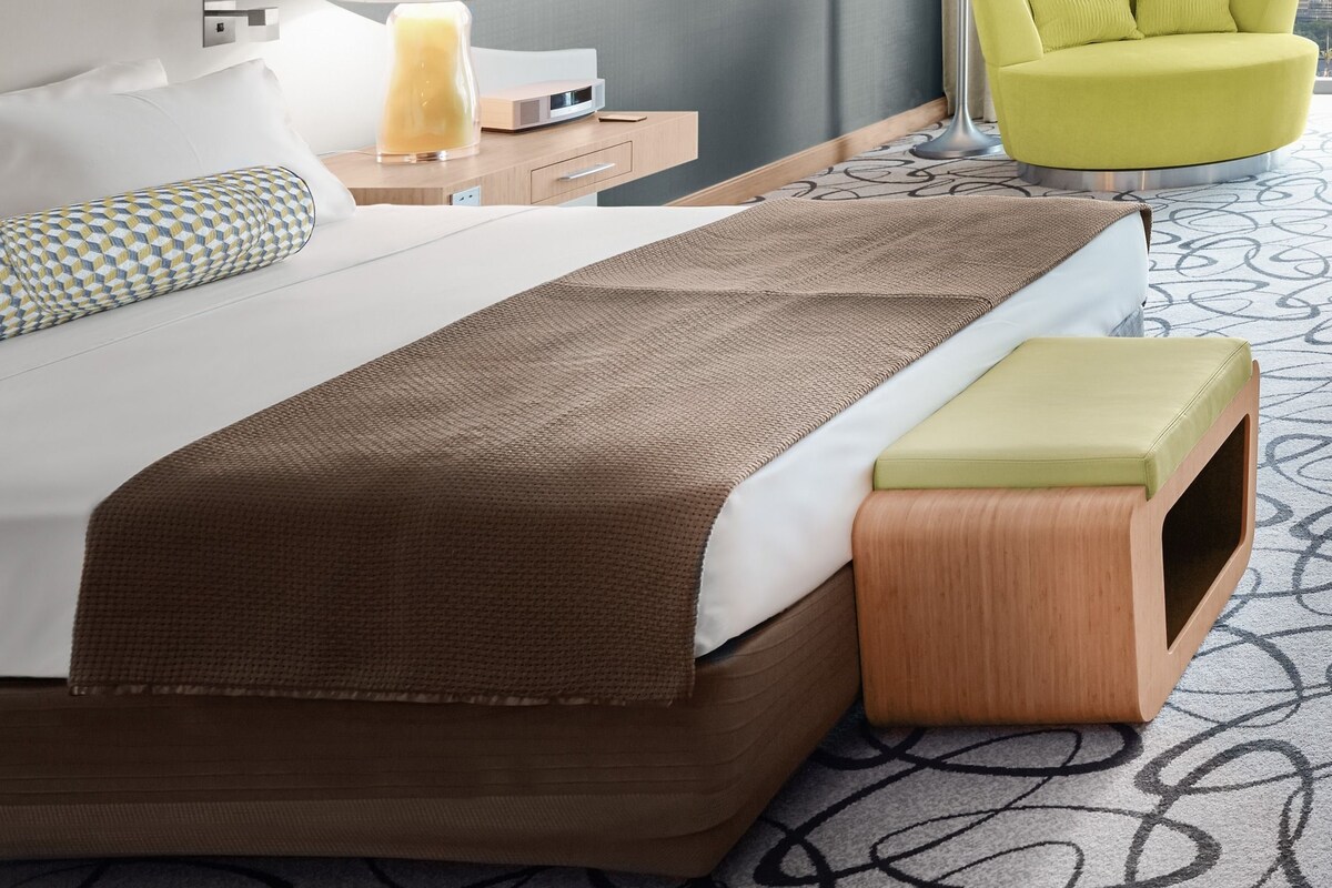 A hotel room with a bed, bedside tables, a lamp, a chair, and a view of the city.