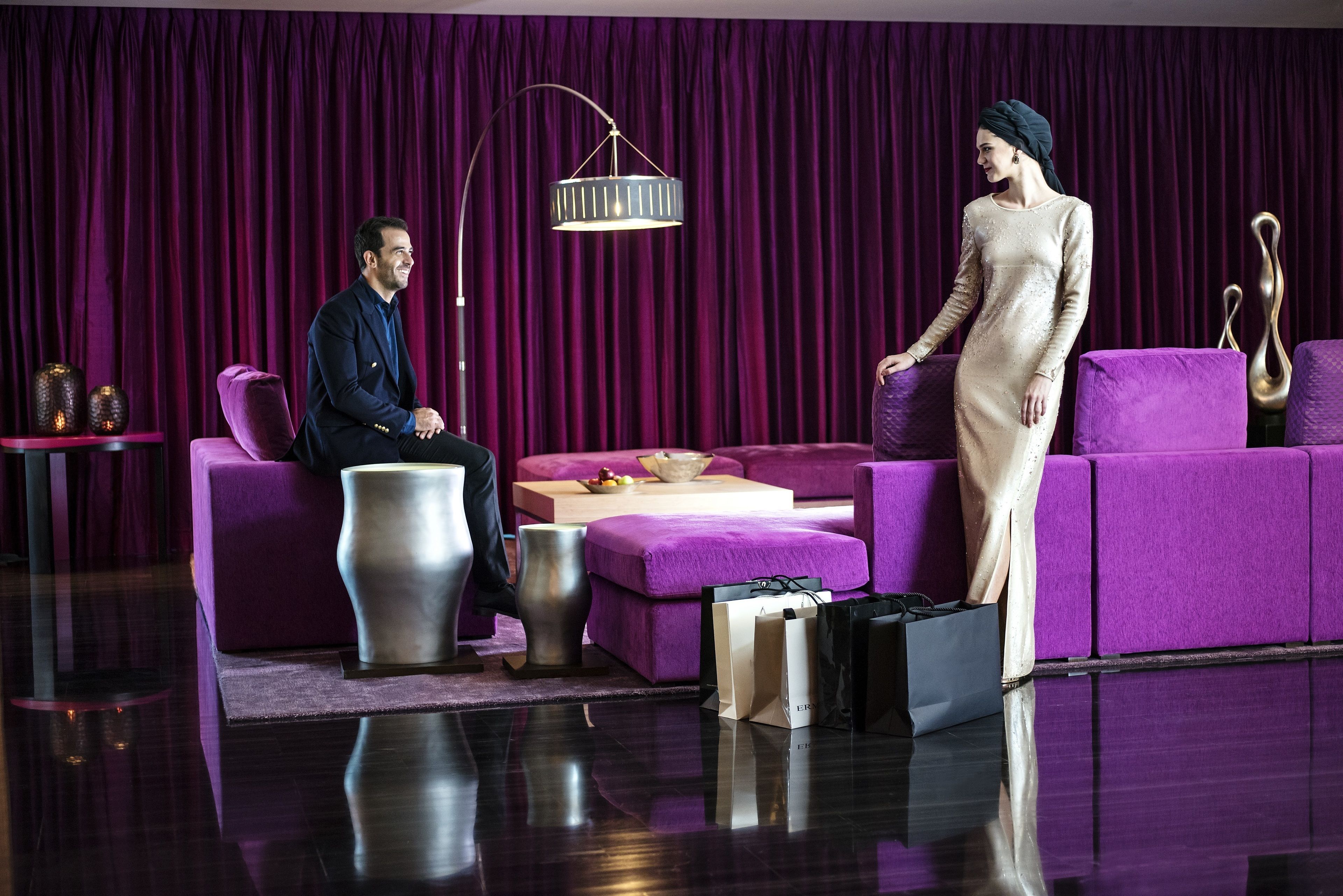 A room with a purple velvet backdrop, a modern chandelier, and a person standing next to a purple sofa.
