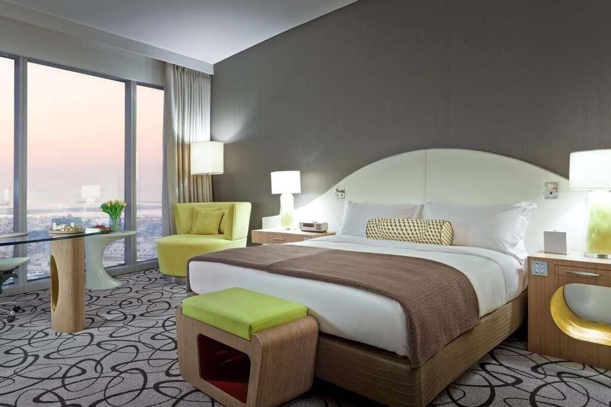 A hotel room with a large bed, a chair, a small table, and a view of the city.