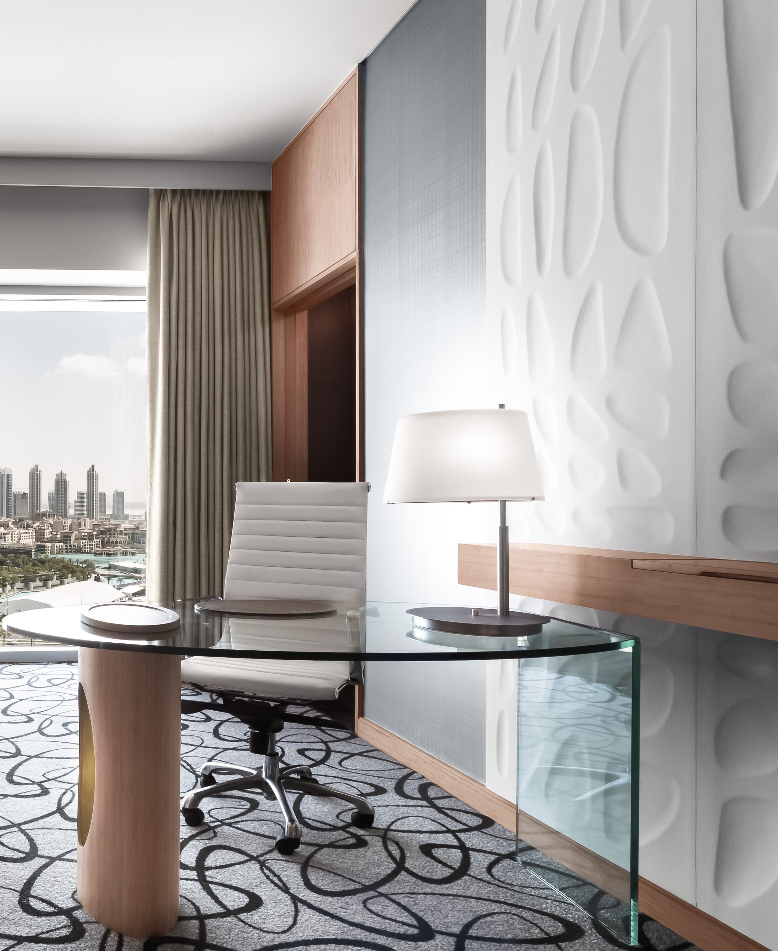 Una habitación de hotel moderna con vista a la ciudad, una mesa de vidrio, una silla blanca y una lámpara.