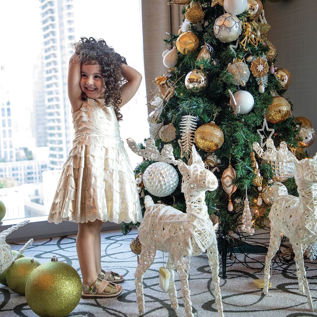 A child standing next to a Christmas tree with white and gold ornaments, surrounded by white reindeer figures.