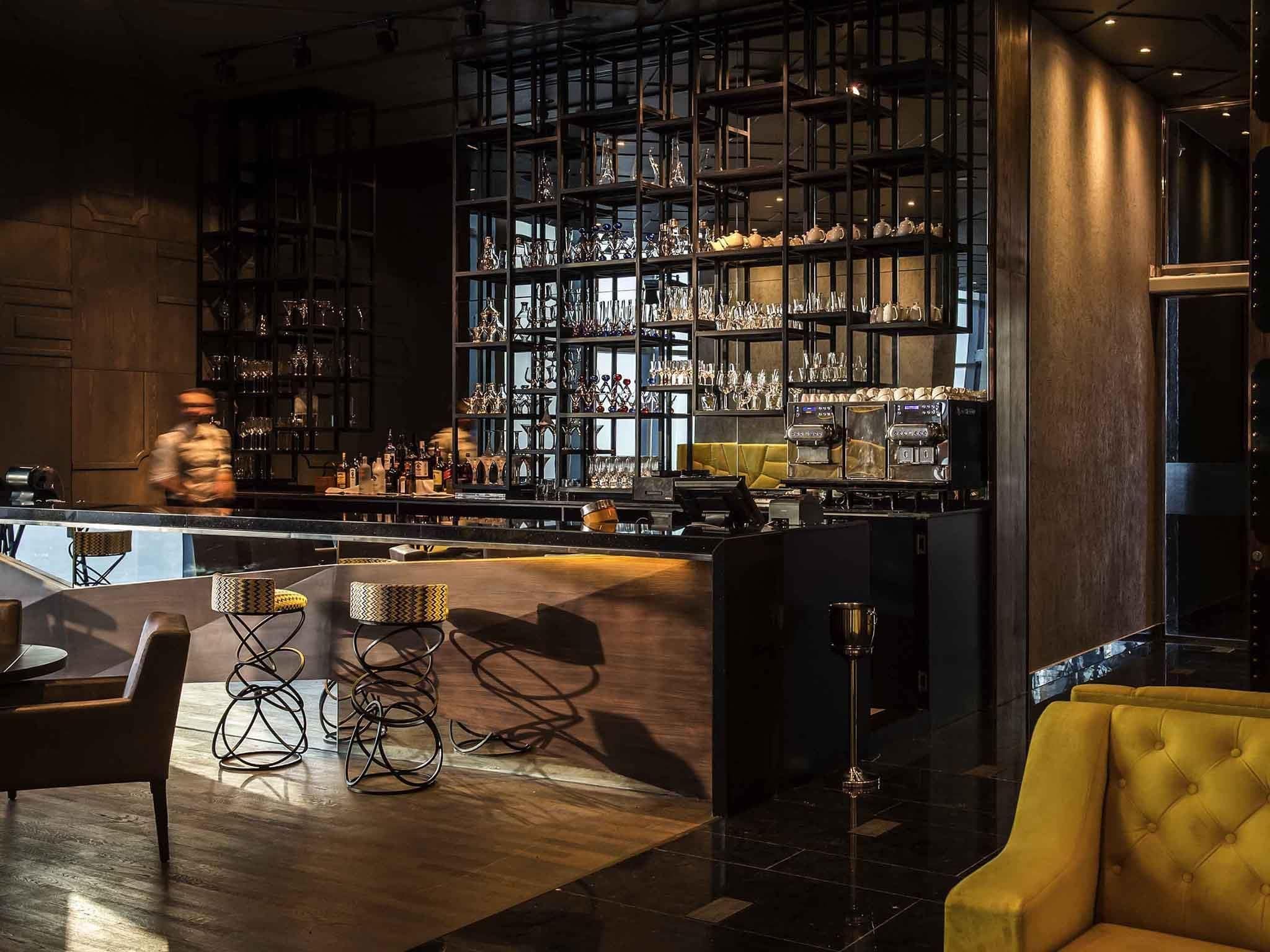 A bar area with shelves of glassware and bottles, a bar counter, and seating with a yellow upholstered chair.