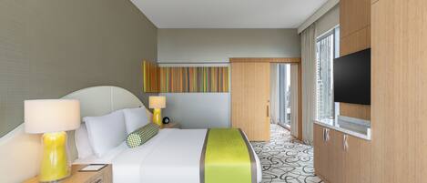 Habitación de hotel con cama, lámparas de noche, televisor, ventana y alfombra estampada.