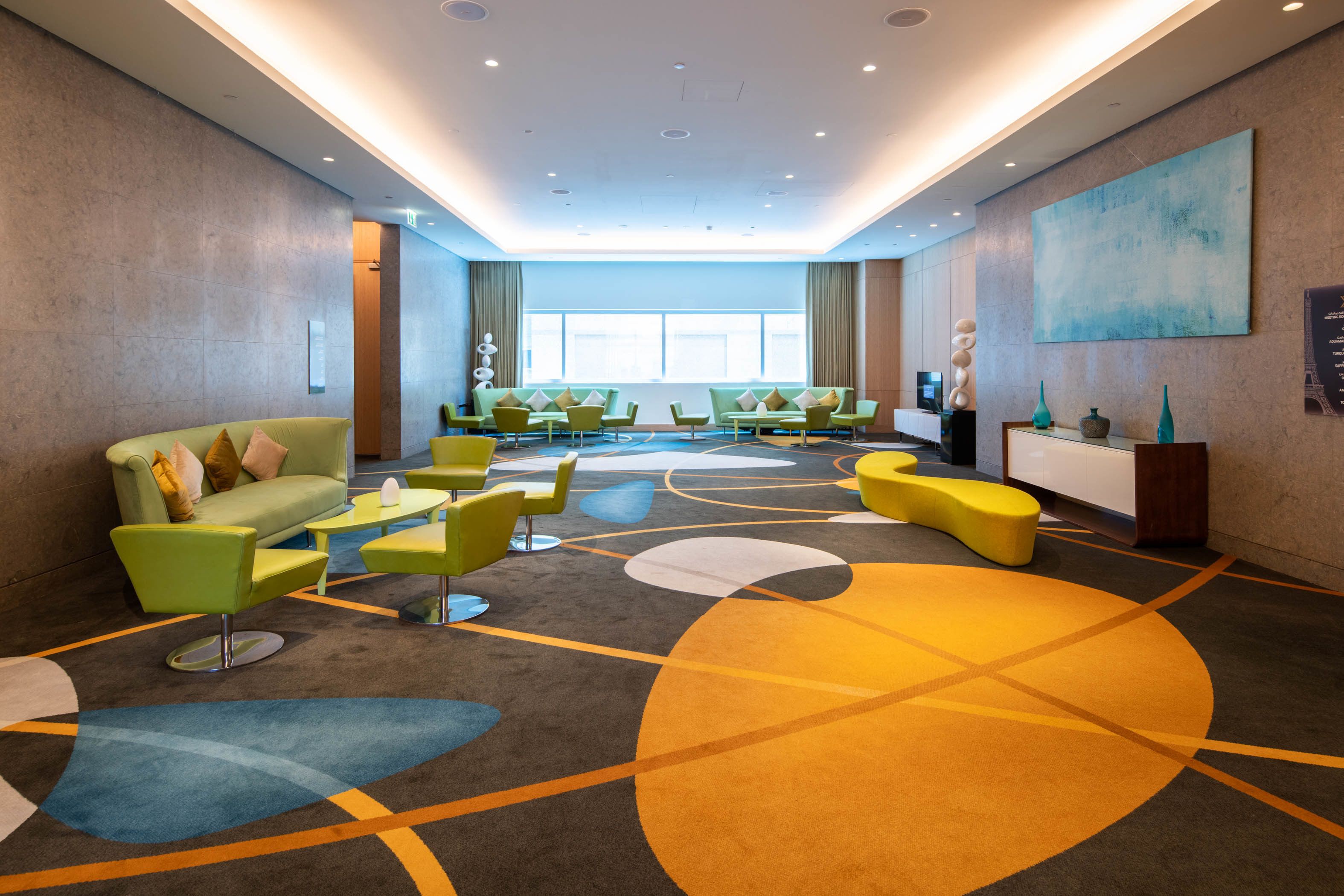 A modern hotel lobby with a central seating area, large windows, and a contemporary art piece on the wall.