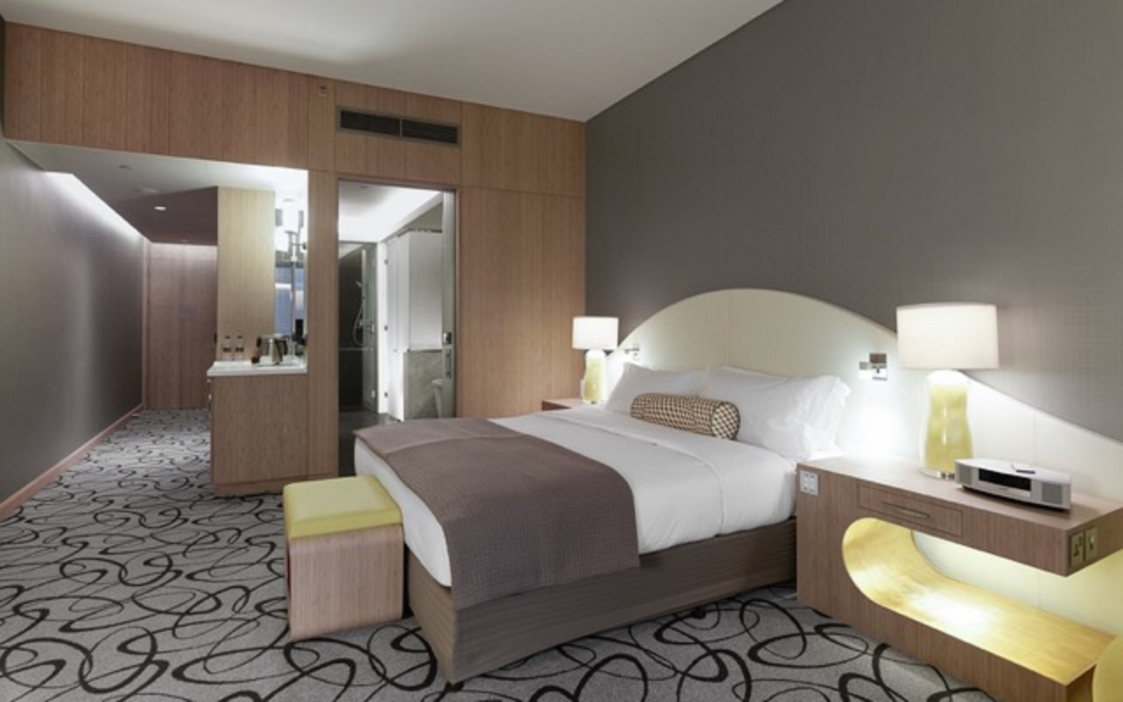 Ett modernt hotellrum med en stor säng, sängbord, ett skrivbord och ett badrum som syns genom en öppen dörr.