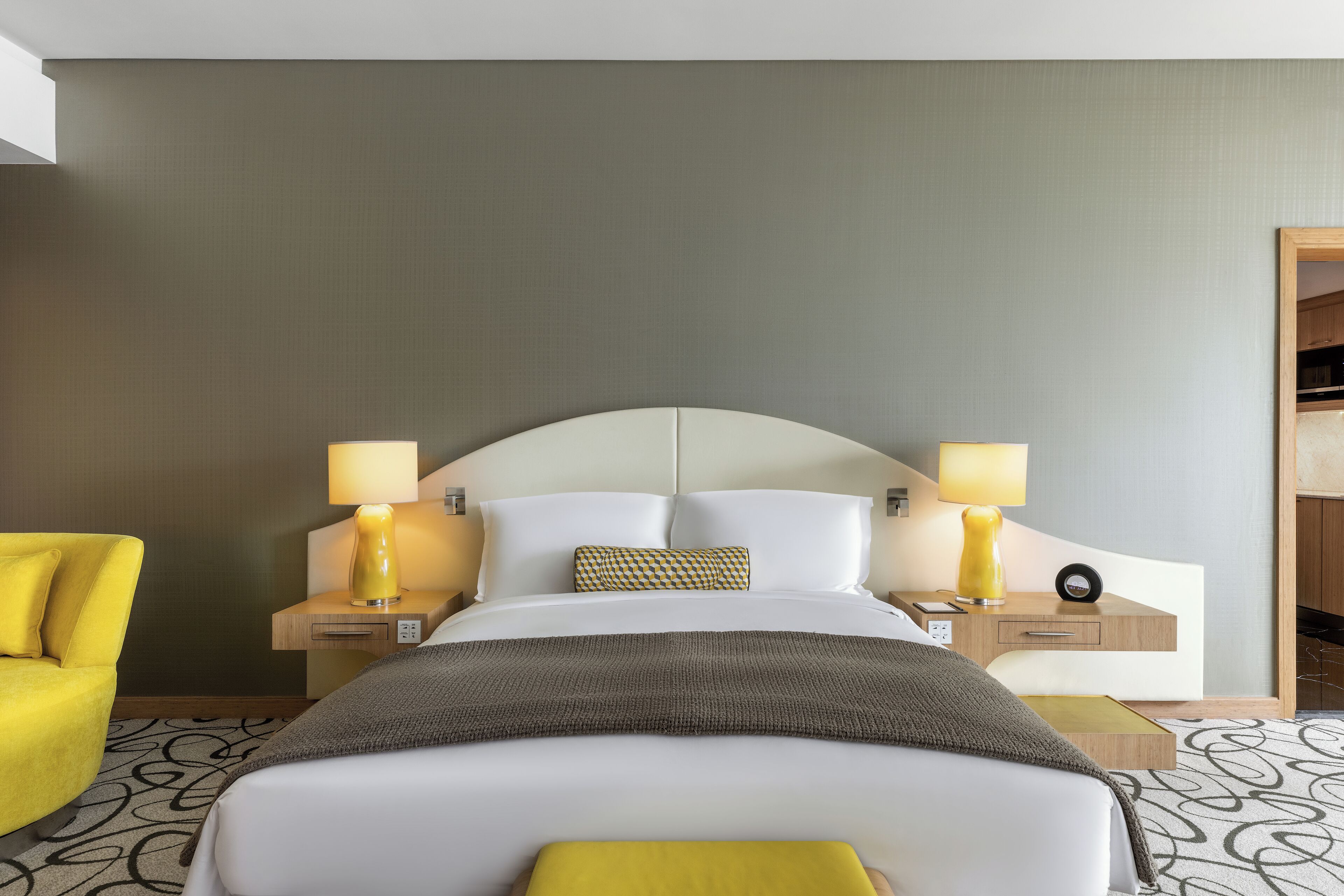 A hotel room with a bed, two bedside tables, a chair, and a nightstand with a lamp.