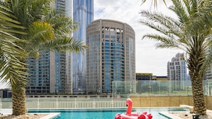 A swimming pool with a red flamingo float, surrounded by palm trees and modern high-rise buildings in the background. - Sofitel Dubai Downtown (Dubai)