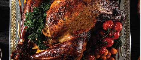 A roasted turkey surrounded by vegetables and nuts on a glass serving tray.