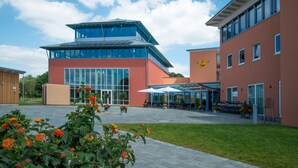 A modern building with a glass facade, a flat roof, and a courtyard with seating and potted plants. - JUFA Hotel Jülich im Brückenkopf-Park (Jülich)