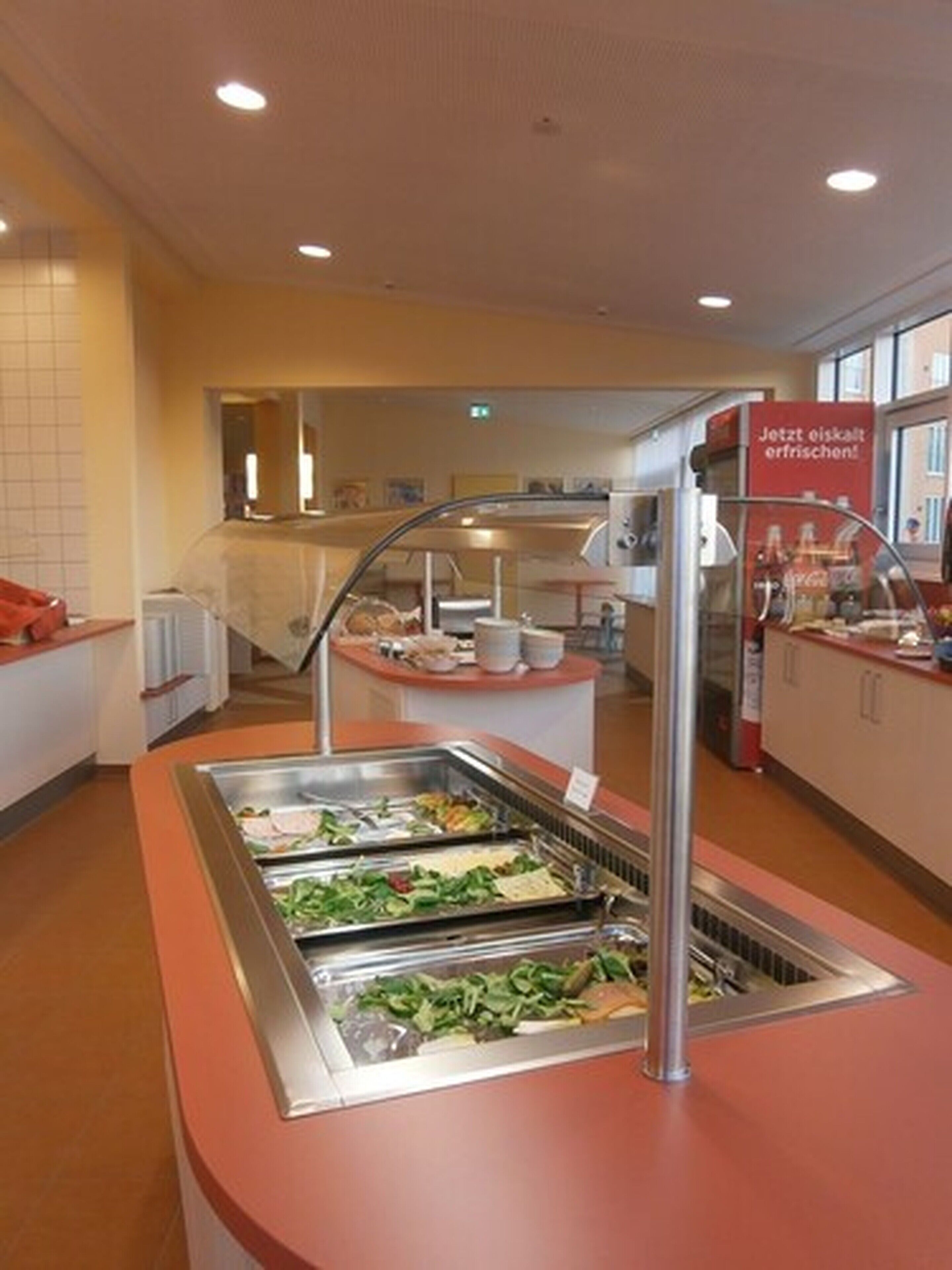 Ein Bereich mit Buffet und verschiedenen Speisen, eine Glastrennwand und ein Schild, das anzeigt, dass das Buffet geöffnet ist.