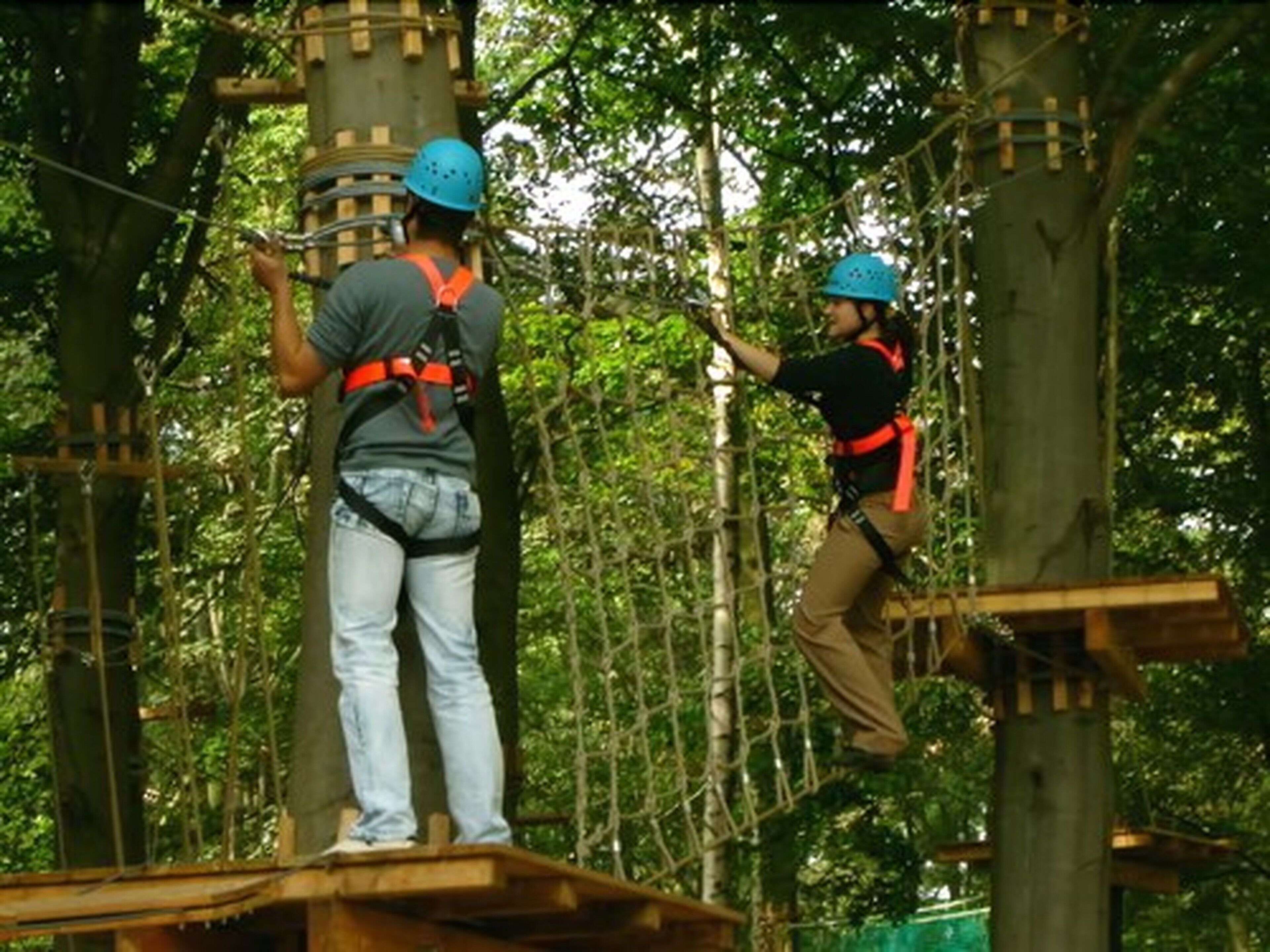 Zwei Personen auf einem Seilparcours in einer bewaldeten Gegend mit Holzbühnen und Seilen.