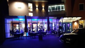 An outdoor seating area with tables and chairs, a car parked nearby, and a building with a sign that reads "JUFA". - JUFA Hotel Jülich im Brückenkopf-Park (Jülich)