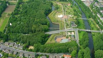 An aerial view of a residential area with a river, a bridge, and a park with a large white building.