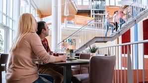 A modern indoor space with a staircase, seating areas, and a view of a cityscape. - JUFA Hotel Jülich im Brückenkopf-Park (Jülich)