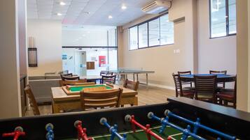 Una habitación con mesa de fútbol, sillas de madera, mesa de tenis de mesa y un sofá.
