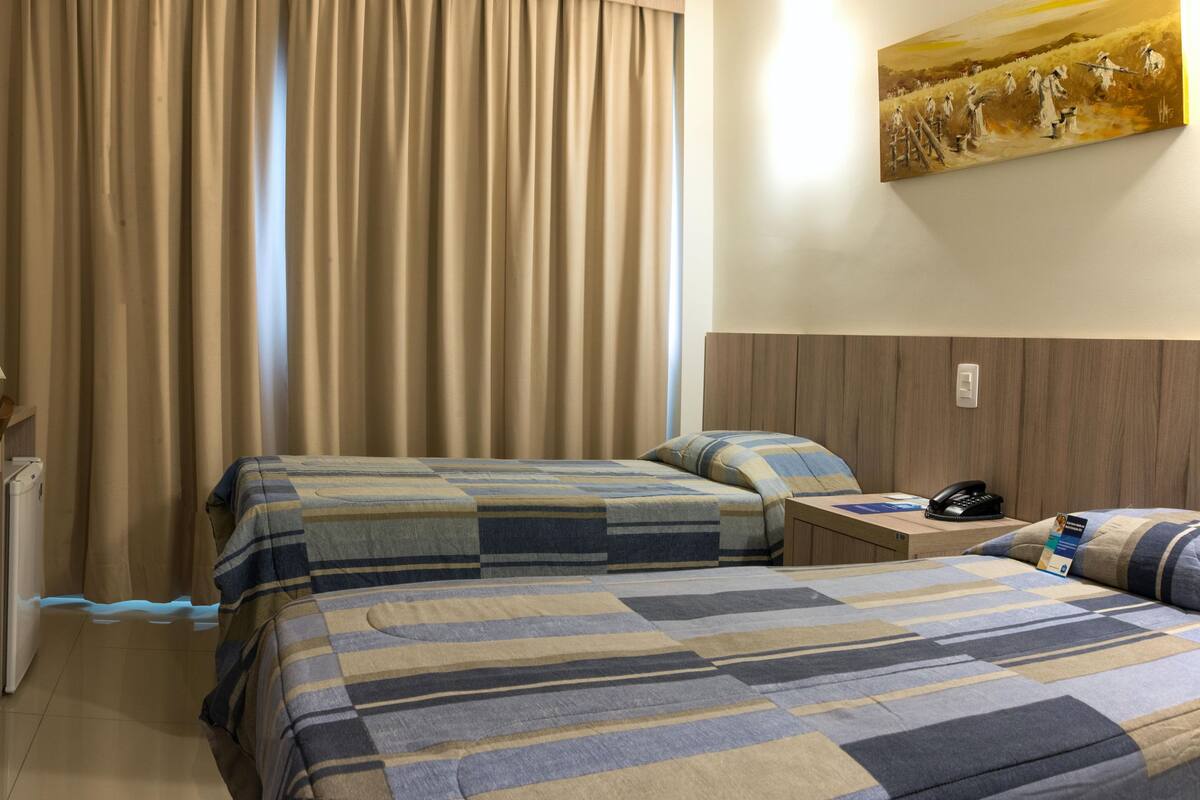 Habitación de hotel con dos camas, un escritorio, una silla, un televisor y un cuadro en la pared.