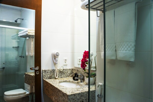 A bathroom with a granite countertop sink, a handheld hair dryer, a glass shower enclosure, and a white toilet.