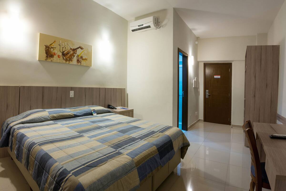 Una habitación de hotel con cama, mesita de noche y un cuadro en la pared.