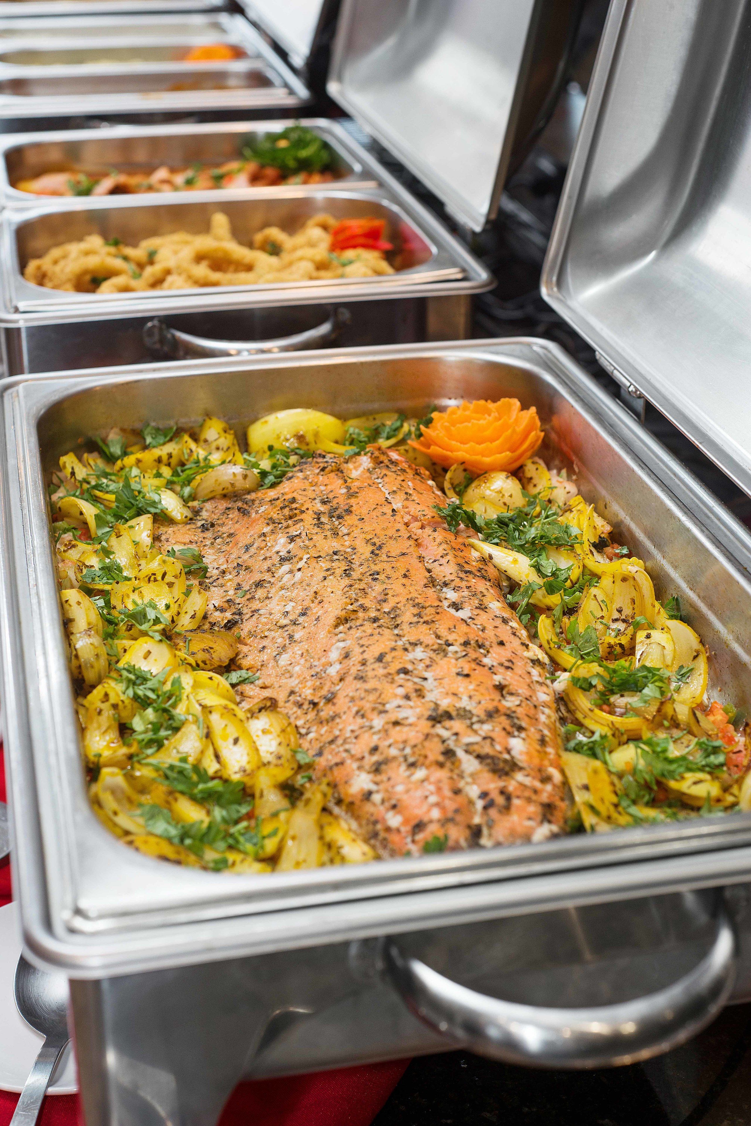 A buffet with various dishes, including a salmon fillet and roasted vegetables.