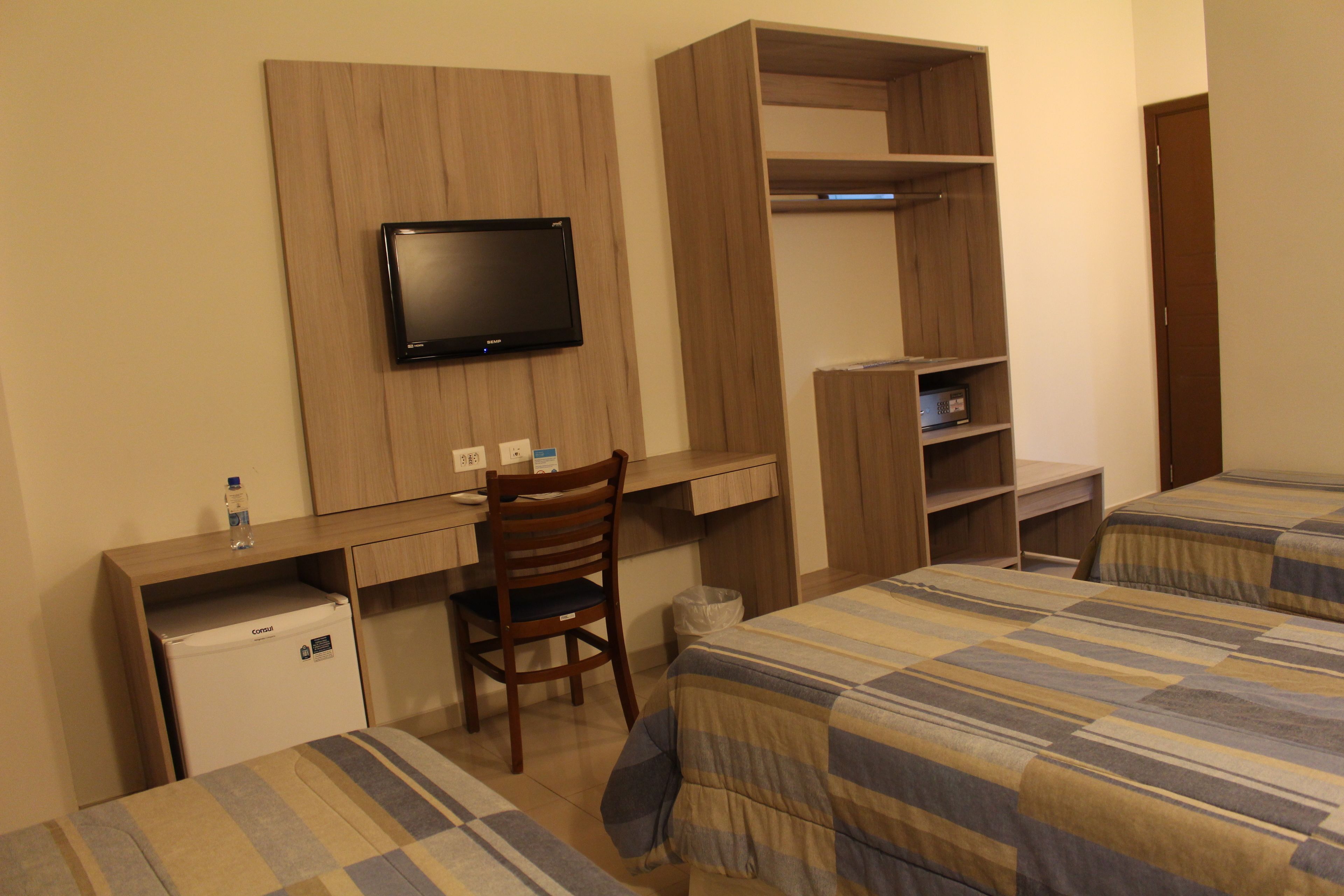 Habitación de hotel con cama, escritorio con silla, televisión montada en la pared y armario.