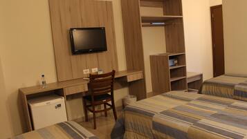 Habitación de hotel con cama, escritorio con silla, televisión montada en la pared y armario.