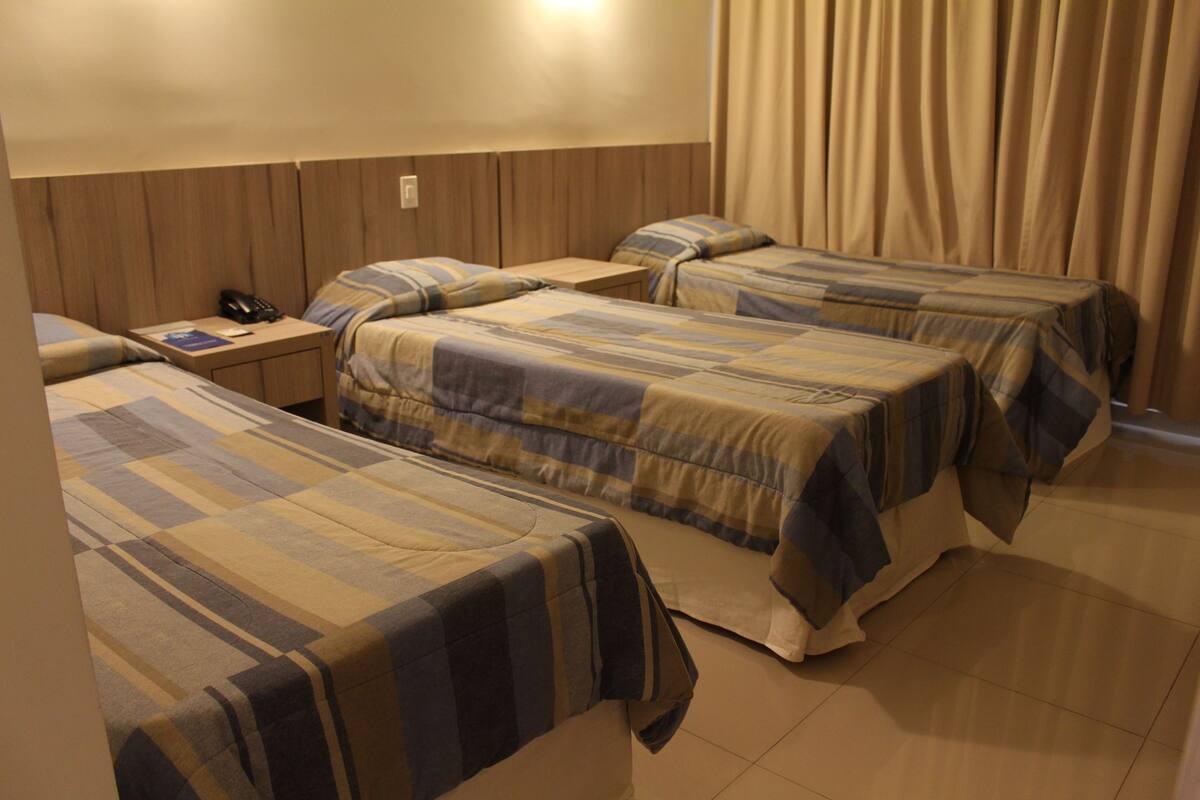 Una habitación de hotel con tres camas, una mesita de noche y un teléfono, y una cortina.