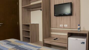 A bedroom with a bed, a TV mounted on the wall, a small fridge, and built-in shelving.