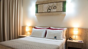 A hotel room with a bed, two bedside tables, a lamp, a wall-mounted artwork, and a curtain. - Hotel Estação 101 (Itajai)