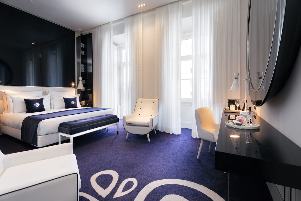 Una habitación de hotel moderna con una cama grande, una zona de estar con una silla, un escritorio y un espejo amplio.