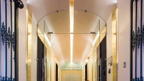 Pasillo de hotel con alfombra que dice "HOTEL PORTUGAL", puertas de vidrio y una zona de estar con sillas.