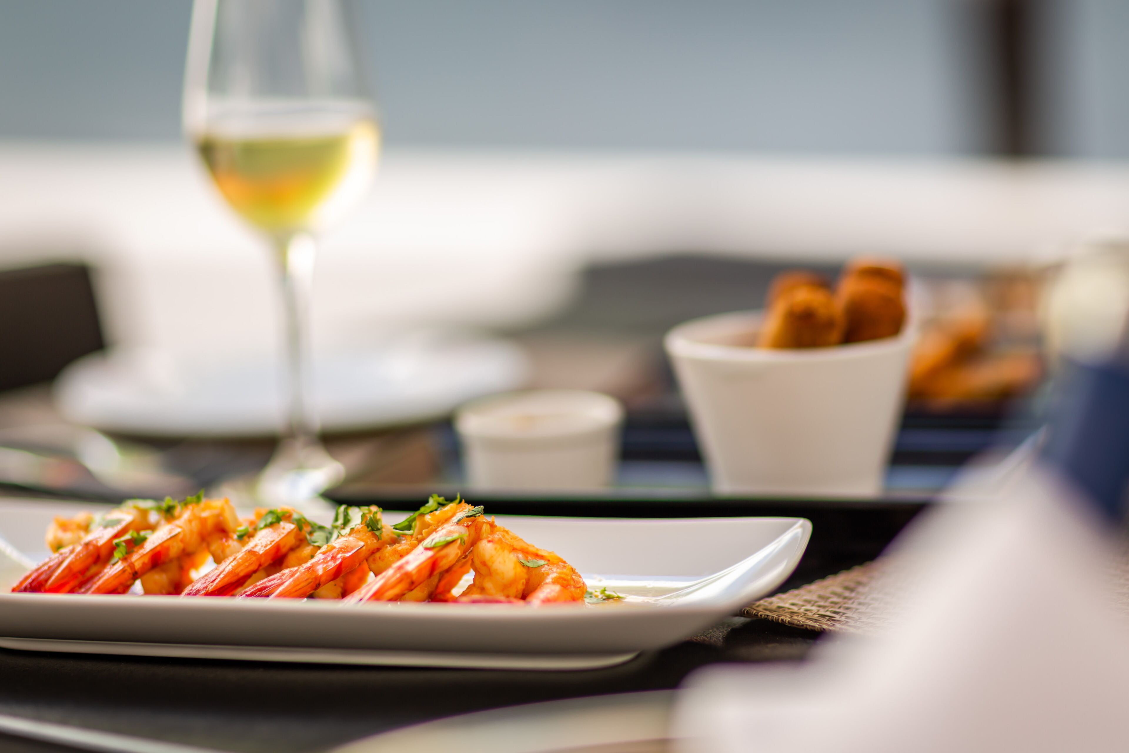 A dining table with a plate of food and a glass of white wine.