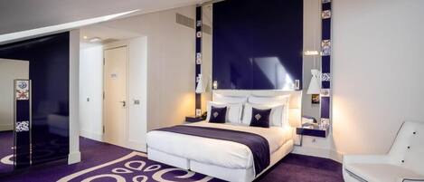 A modern bedroom with a large bed, a white chair, and a unique purple carpet design.
