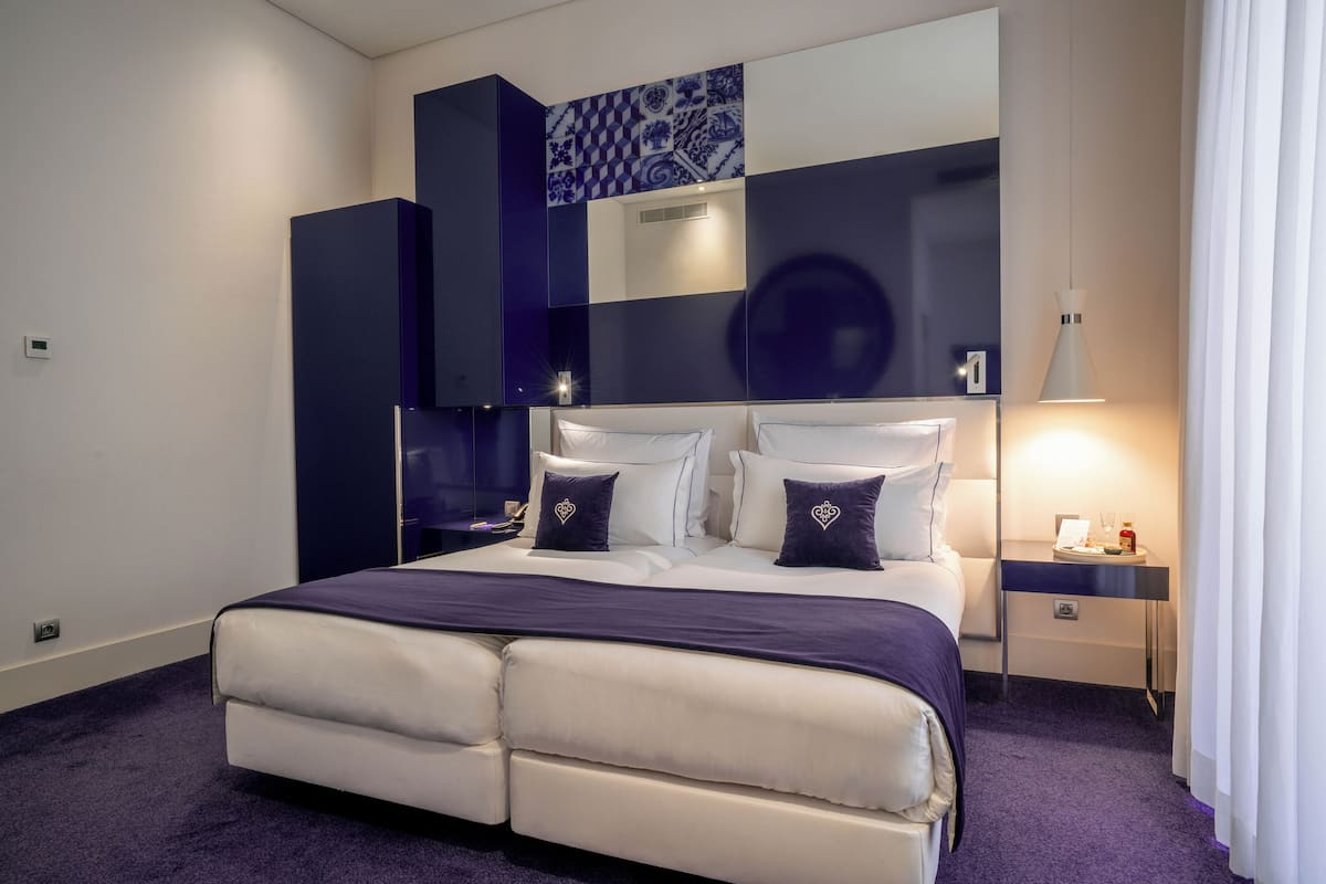 Una habitación de hotel moderna con una cama grande, una mesita de noche y otra mesita auxiliar.
