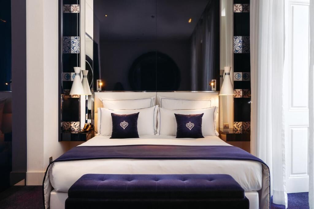 Una cama con cabecera blanca, dos almohadas con diseño de corazones y una colcha azul oscuro.