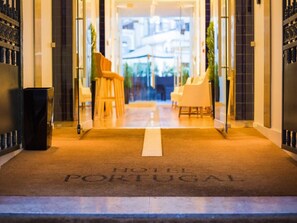 A hotel entrance with a carpet reading "HOTEL PORTUGAL" and a glass door leading to a seating area with chairs. - Portugal Boutique Hotel (Lisbon)