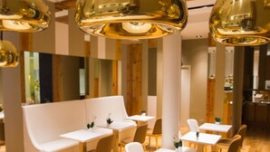 Un interior moderno con sofás blancos, mesas de madera e iluminación colgante dorada.