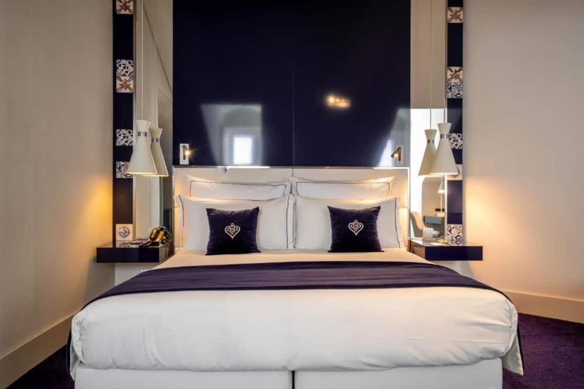 Una habitación de hotel con una cama grande, dos mesitas de noche y un cabecero oscuro.
