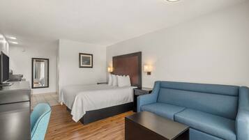A hotel room with a bed, a blue sofa, a desk, a chair, and a flat-screen TV.